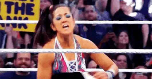 a female wrestler is standing in a wrestling ring with a crowd watching .