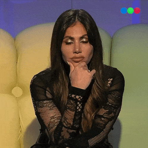 a woman in a black lace top is sitting on a couch with her hand on her chin