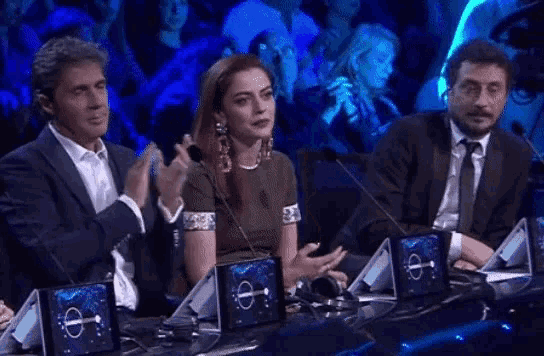 a group of people are sitting at a table with microphones and a woman is applauding