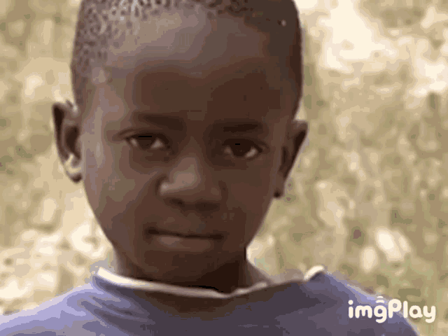 a young boy in a blue shirt is looking at the camera and making a funny face .