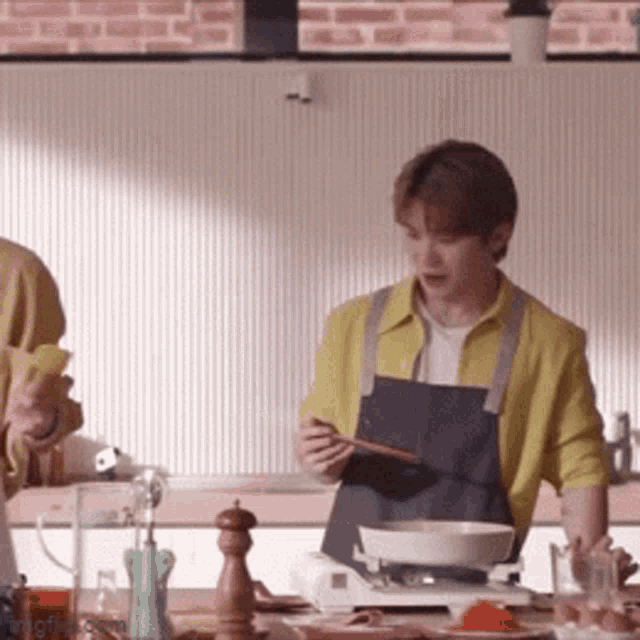 a man in a yellow shirt is cooking in a kitchen while another man looks on .