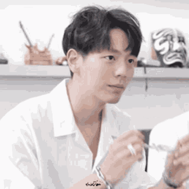 a young man in a white shirt is holding a pair of glasses and a pen .