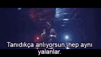 a man is standing in front of a microphone in a dark room with a caption in a foreign language .