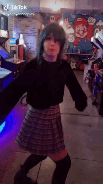 a girl in a plaid skirt is dancing in an arcade with a mural of mario on the wall behind her