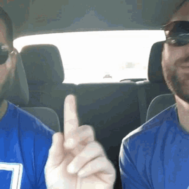 two men wearing sunglasses are sitting in a car and one is pointing up