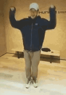 a man in a blue jacket and hat is standing with his arms up in the air .