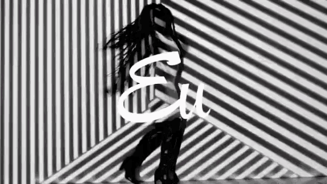 a black and white photo of a woman dancing in front of a striped wall with the word eu written on it .