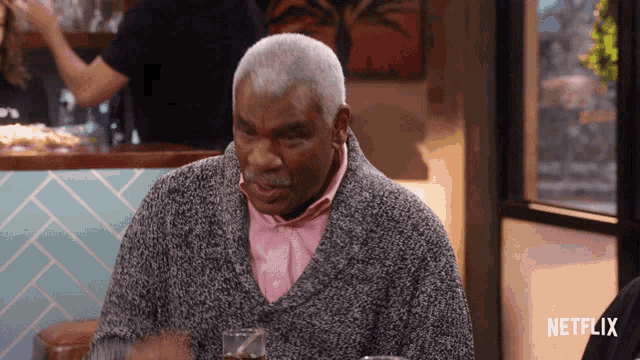 a man in a grey sweater is sitting at a table with a netflix logo in the corner