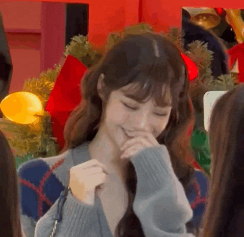 a woman in a sweater is smiling and covering her mouth with her hand in front of a christmas tree .