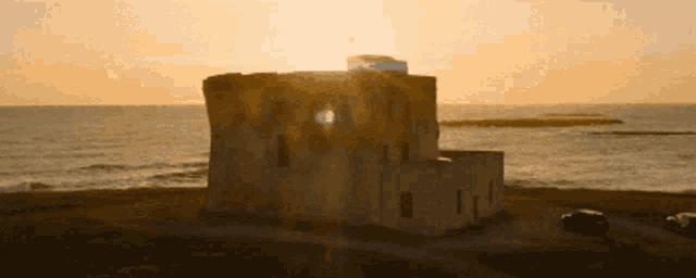 the sun is setting behind a building on the coast