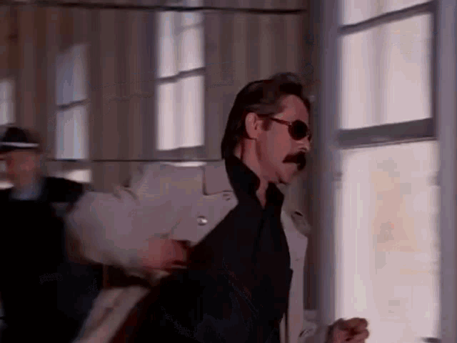 a man with a mustache and sunglasses is walking through a doorway .