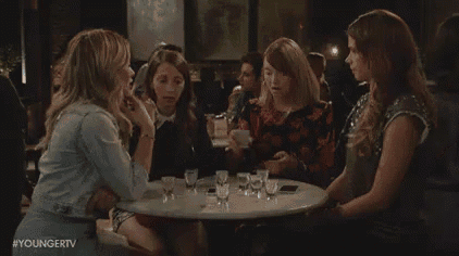 a group of women are sitting around a table talking to each other .