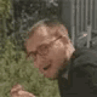 a man wearing glasses and a black shirt is smiling and looking at something .