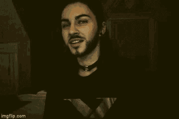 a man with long hair and a beard wearing a choker is smiling .