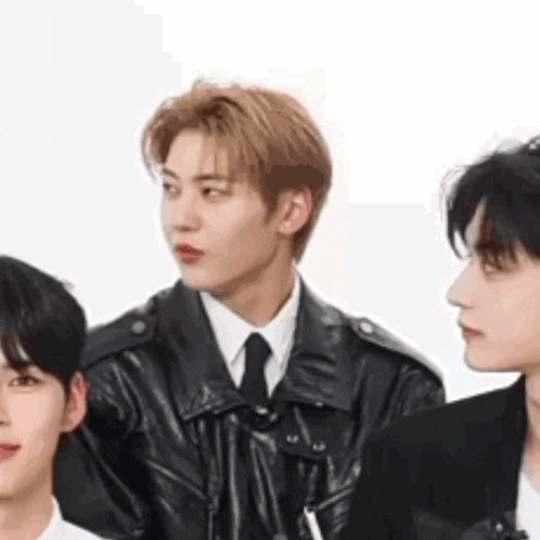 a group of young men are standing next to each other and one of them is wearing a leather jacket .