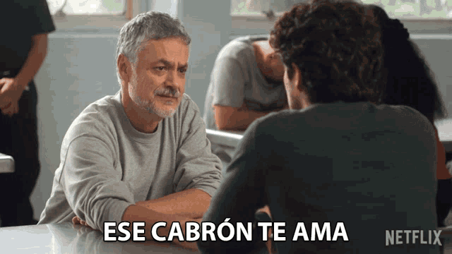 a man sitting at a table with the words ese cabron te ama written below him
