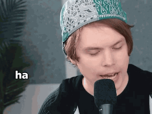 a man wearing a bandana and a hat is singing into a microphone with the word ha below him .