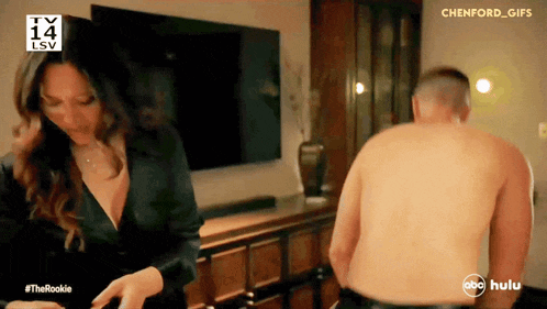 a man without a shirt is standing next to a woman in front of a television screen that says lsv 14