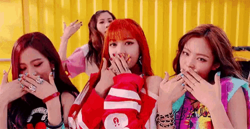 a group of girls are standing next to each other and covering their faces with their hands .