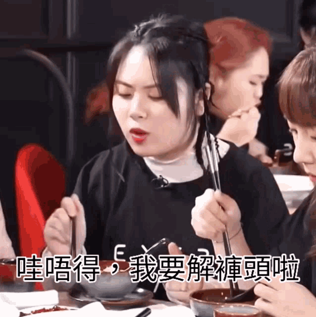 a group of people are sitting at a table eating food with chopsticks and chinese writing