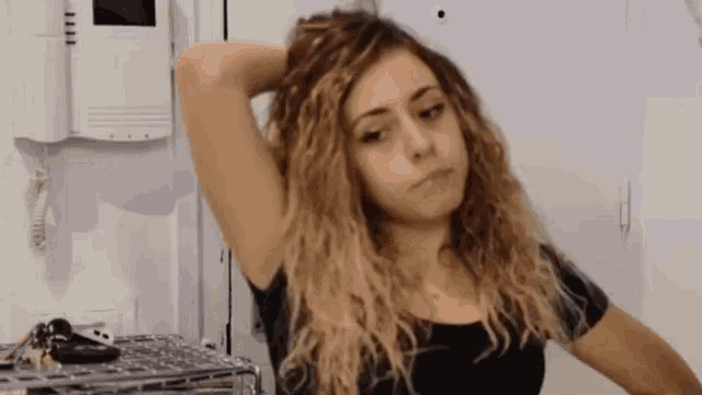 a woman with curly hair is standing in front of a door holding her hair .