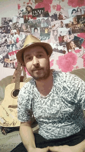 a man wearing a hat sits in front of a guitar with a signature on it