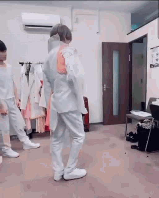 a group of people are standing in a room with clothes hanging on a rack .