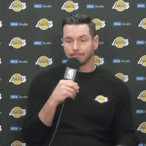 a man is holding a microphone in front of a wall with lakers logos