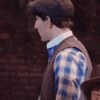 a man wearing a hat and vest is standing in front of a wall .