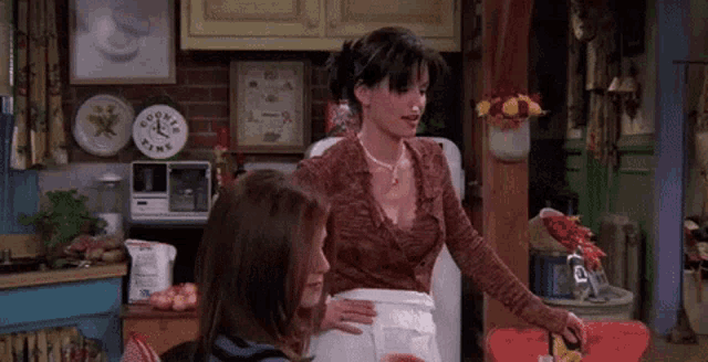 two women are standing in a kitchen with a clock on the wall that says cooker time
