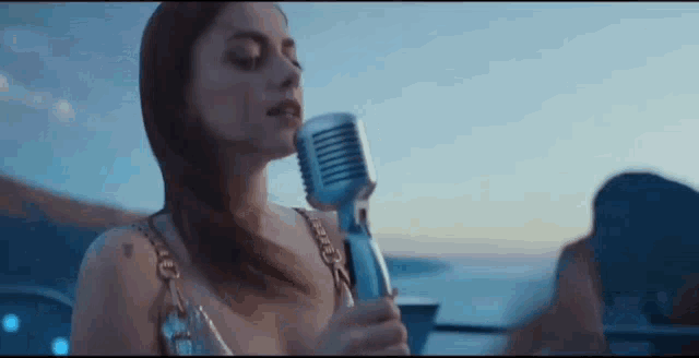 a woman is singing into a microphone while standing in front of the ocean .
