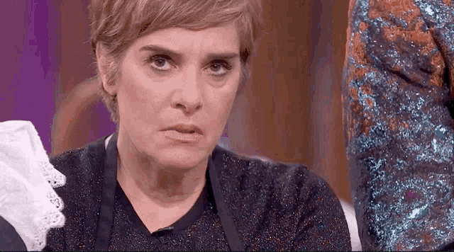 a woman with short hair is making a funny face while wearing an apron and a sweater .