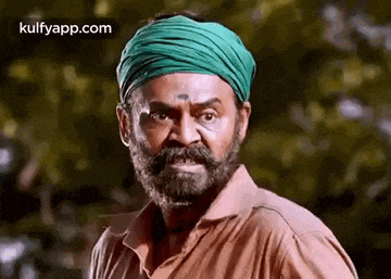 a man with a beard and mustache wearing a green turban is making a funny face .
