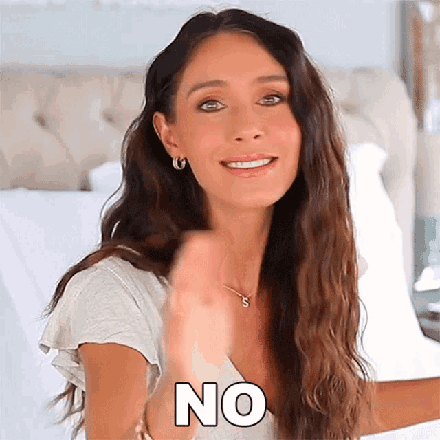 a woman is sitting on a bed and smiling while holding her hand up and saying no .
