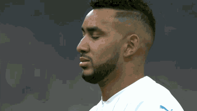 a man with a beard is wearing a white shirt with a blue puma on the sleeve