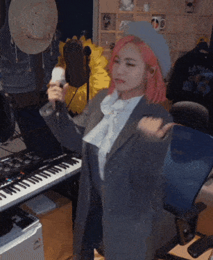 a woman with pink hair is singing into a microphone in front of a piano