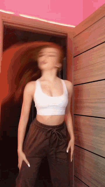 a woman in a crop top and brown pants is dancing in a room .