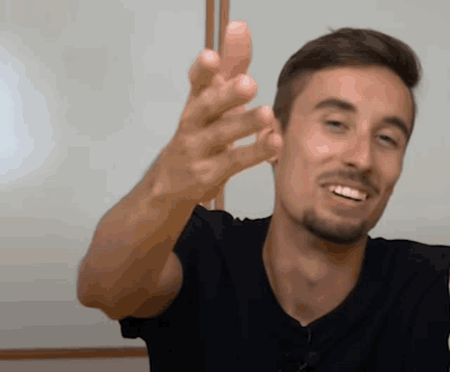 a man with a beard is smiling and waving his hand in front of a whiteboard .