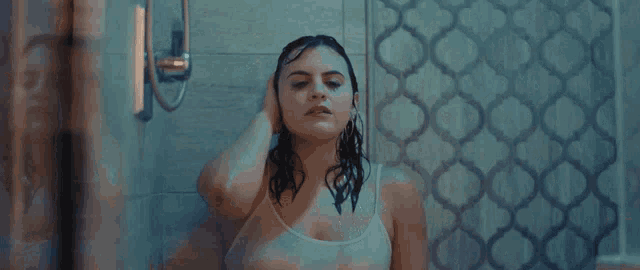 a woman in a white tank top is taking a shower with her hair wet .