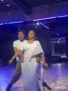 a man and a woman are dancing together in a dance studio . the woman is wearing a white sari .