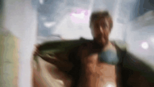 a man without a shirt is standing in front of a window with his arms outstretched .