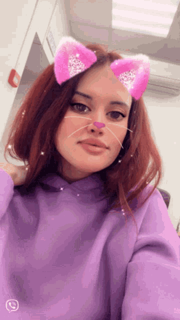 a woman wearing a purple hoodie and pink cat ears takes a selfie