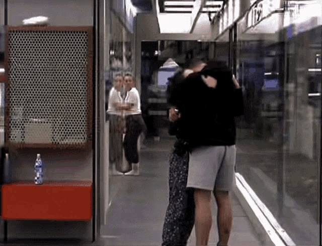 a man and a woman are hugging in a hallway with a bottle of water on a shelf
