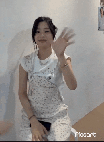 a girl in overalls is waving her hand in front of a wall with picsart on it