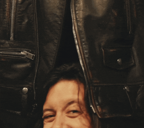 a person covering their face with their hands in front of a black leather jacket