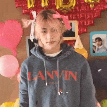 a young man wearing a lanvin hoodie is standing in front of balloons and pictures .