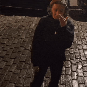 a woman standing on a cobblestone street with her hand on her face