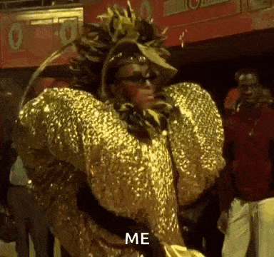 a woman in a gold costume is standing in front of a crowd and says `` me '' .