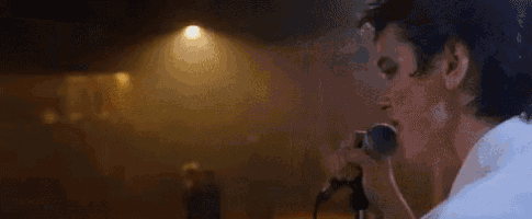 a man is singing into a microphone in a dark room while people dance in the background .