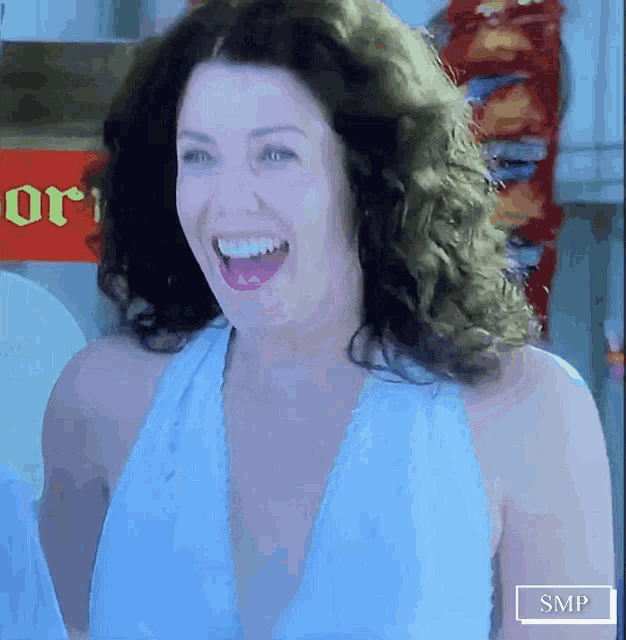 a woman in a blue dress is smiling in front of a red sign that says ori